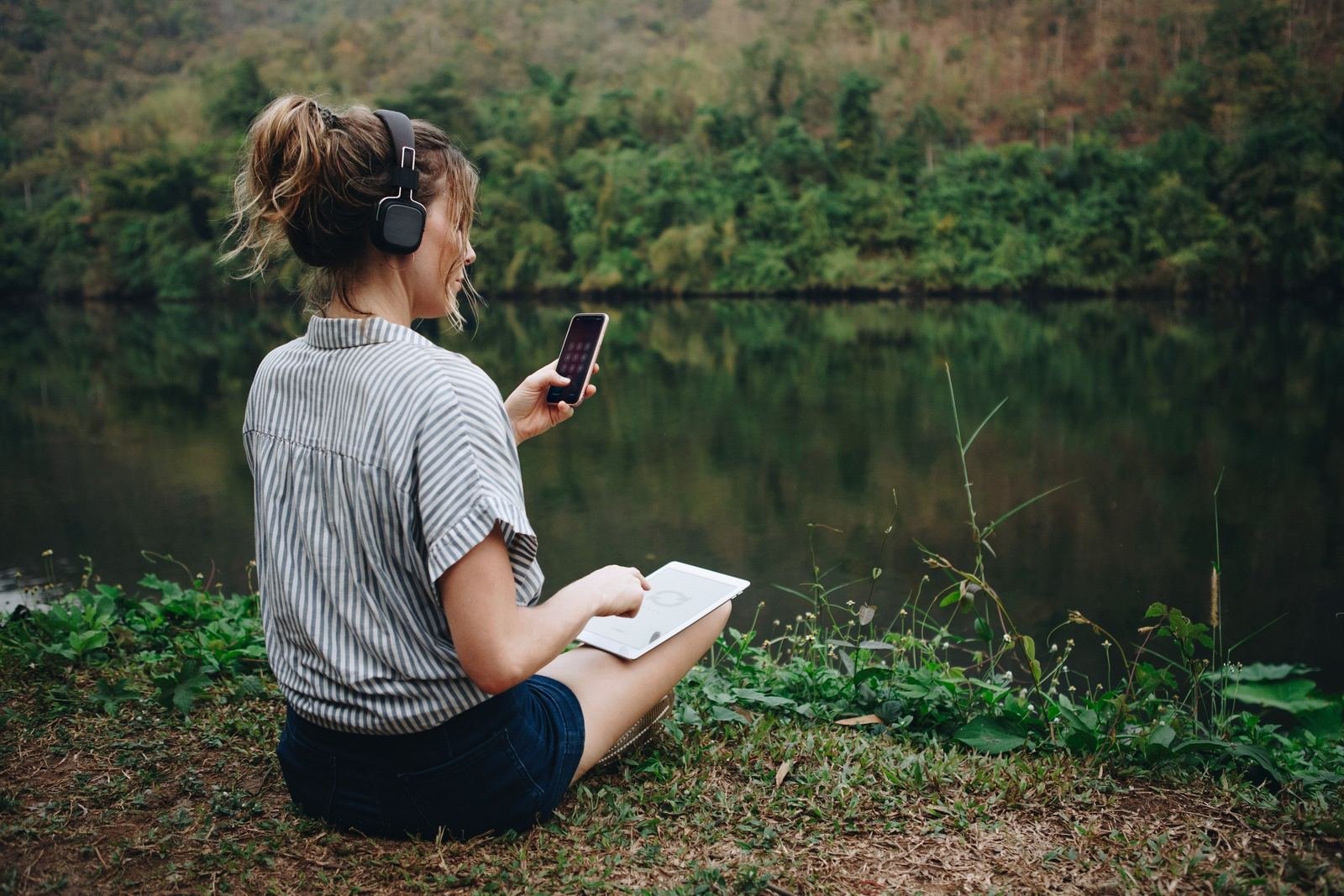 Una mujer escucha música sentada junto a un lago