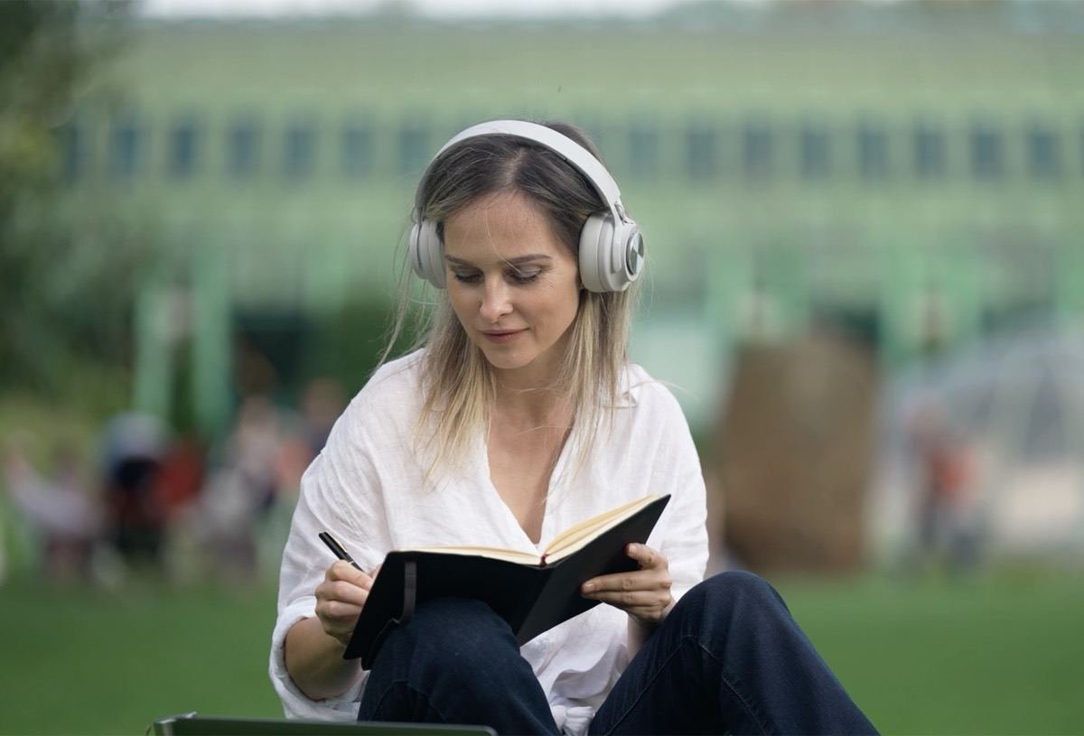 Una mujer escribiendo en un cuaderno al aire libre, con auriculares