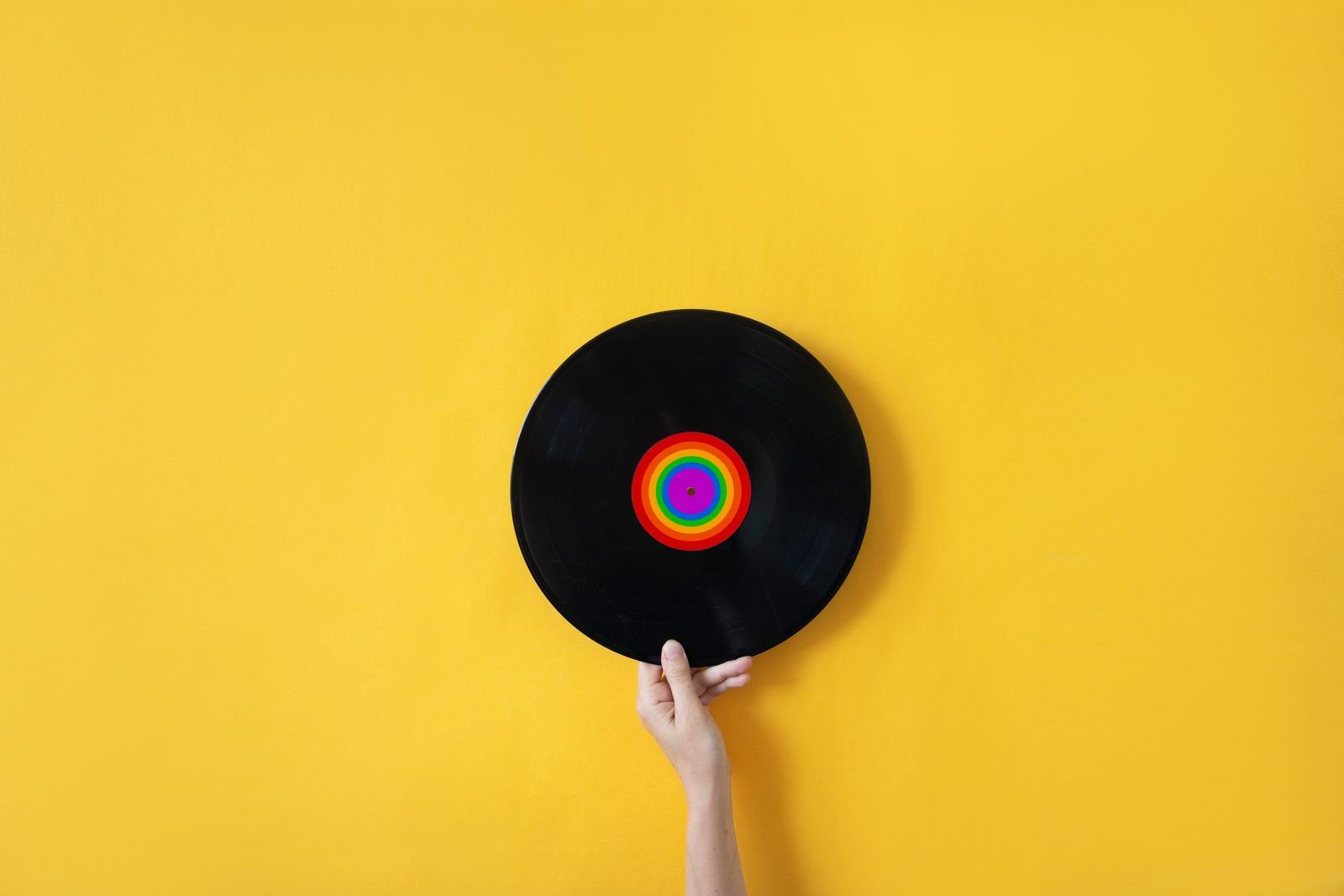 Una mano sostiene un vinilo sobre un fondo amarillo